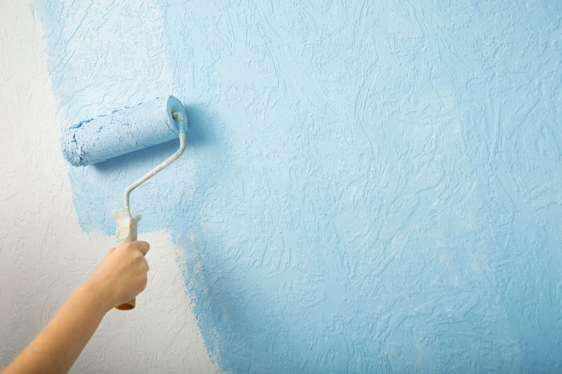A person is painting a wall with a blue paint roller.