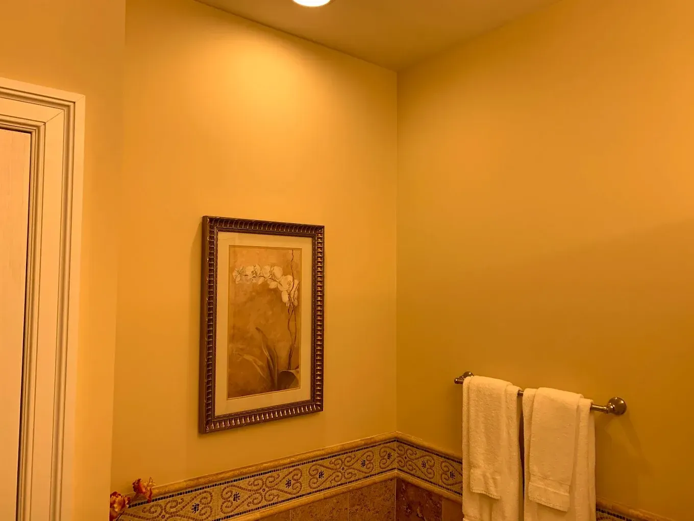 A bathroom with yellow walls and a picture on the wall above the bathtub.