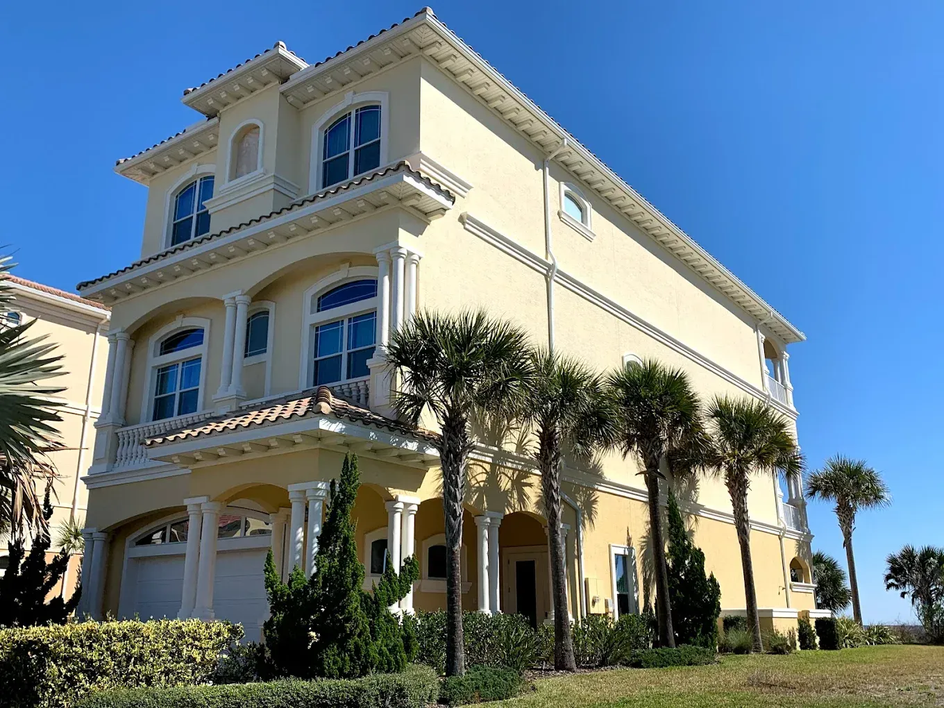 A large yellow house with palm trees in front of it.