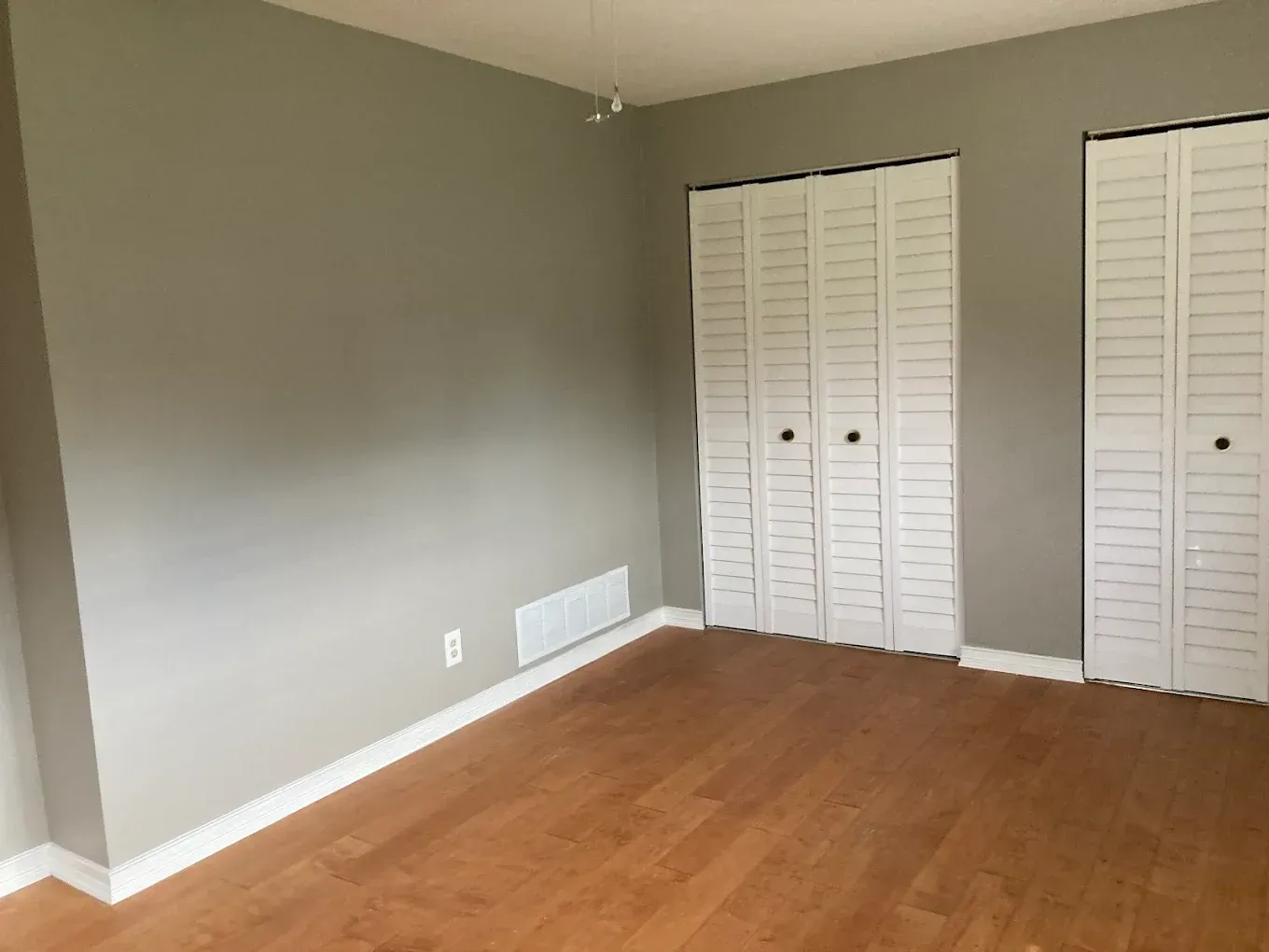 An empty bedroom with hardwood floors and white closet doors.