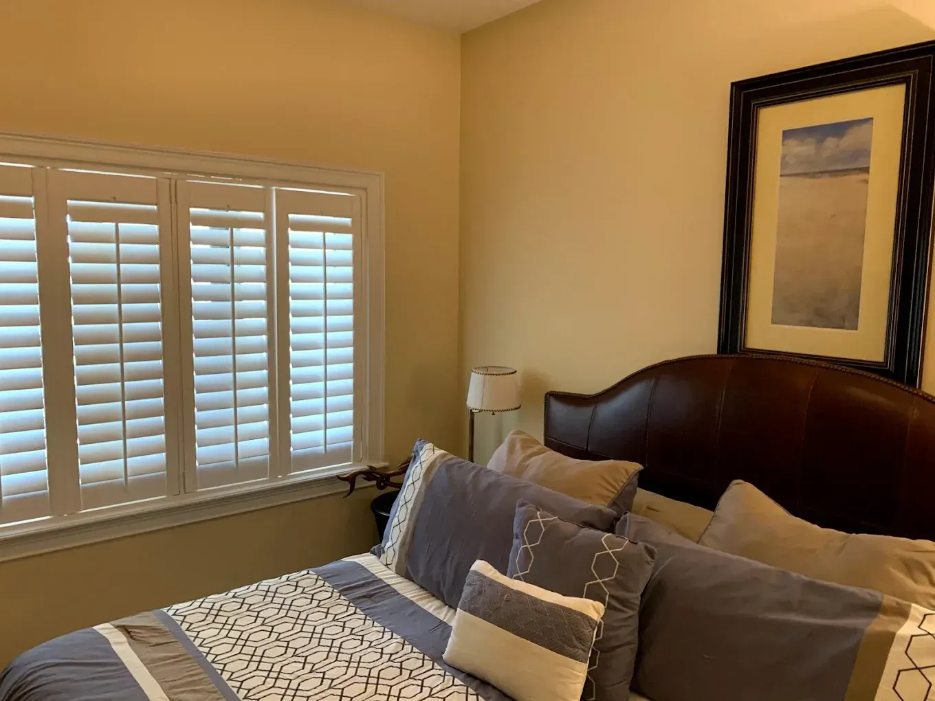 A bedroom with a bed , shutters and a picture on the wall.