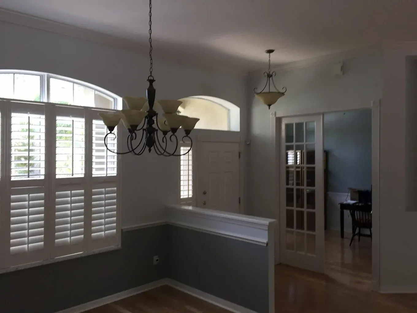 An empty dining room with shutters and a chandelier