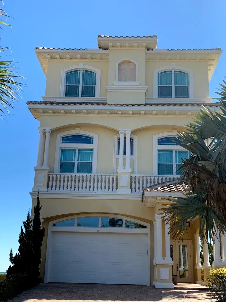A large yellow house with a white garage door and a balcony.