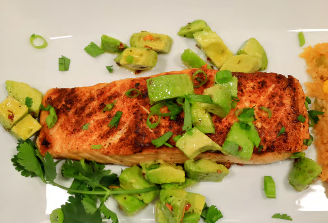 A white plate topped with a piece of salmon and avocado slices.