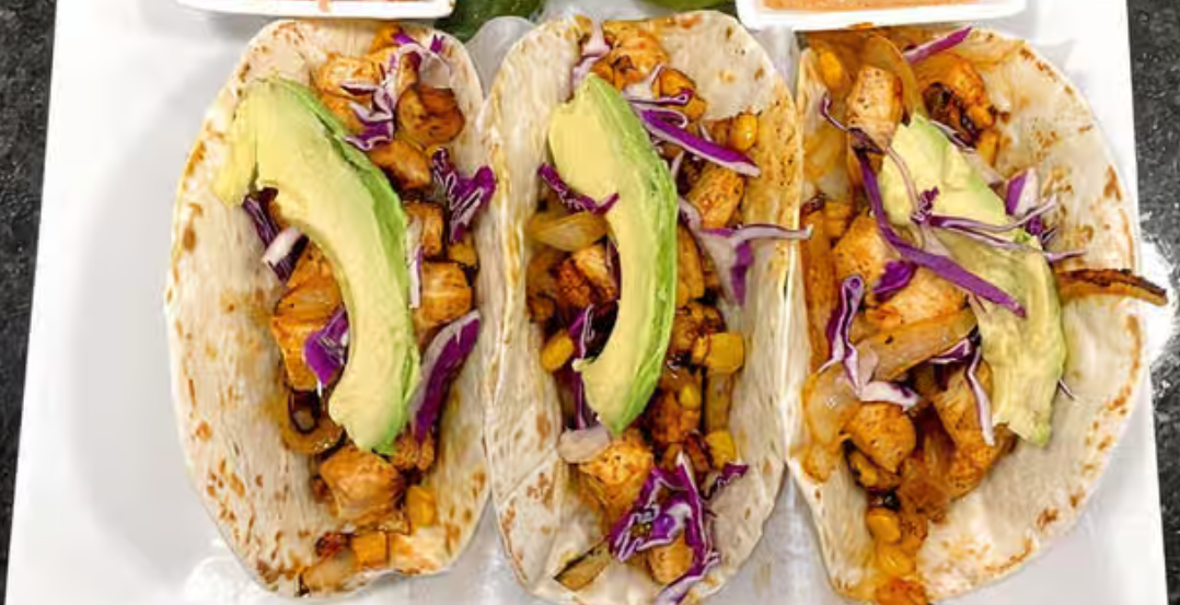 Three tacos with avocado , cabbage , and chicken on a white plate.