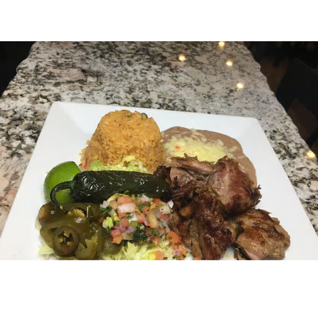 A white plate topped with meat , rice , beans and vegetables on a counter.