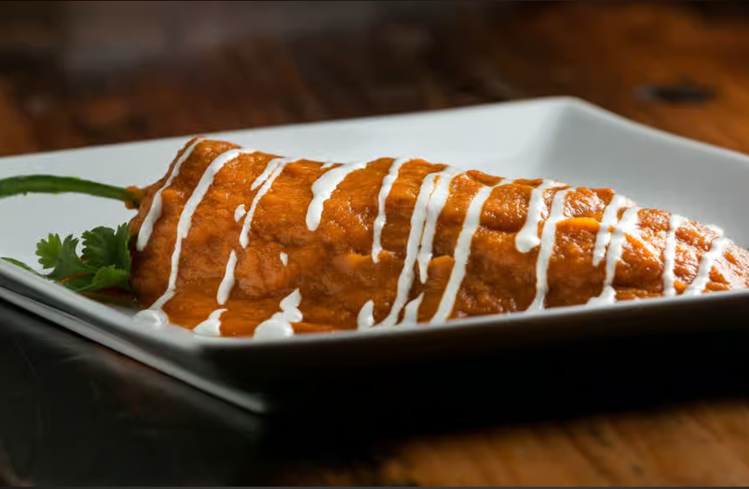 A white plate topped with a pepper covered in sauce and white sauce.