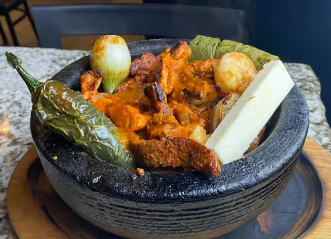 A bowl of food with meat , peppers , onions and cheese on a table.