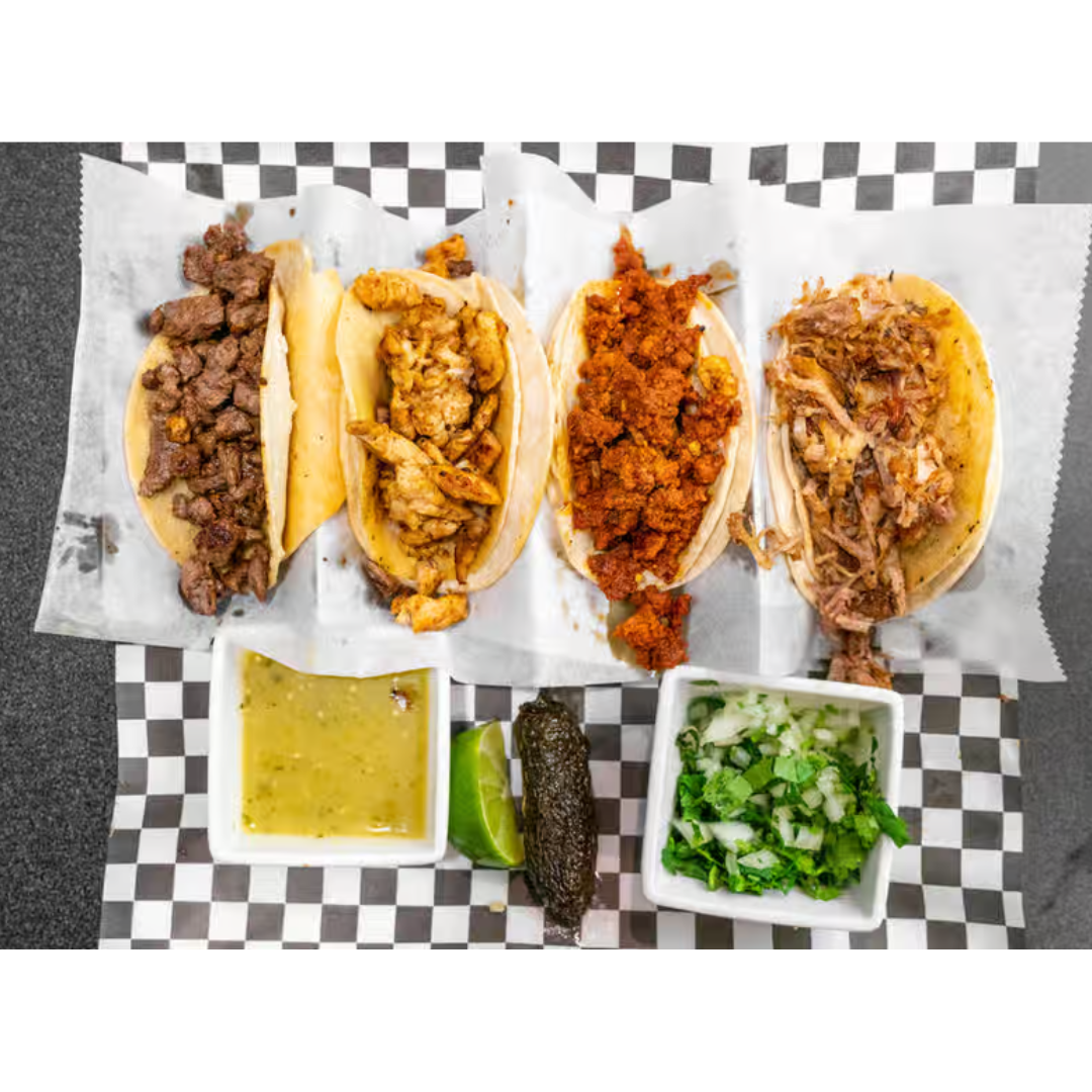 A variety of tacos are sitting on a checkered paper on a table.