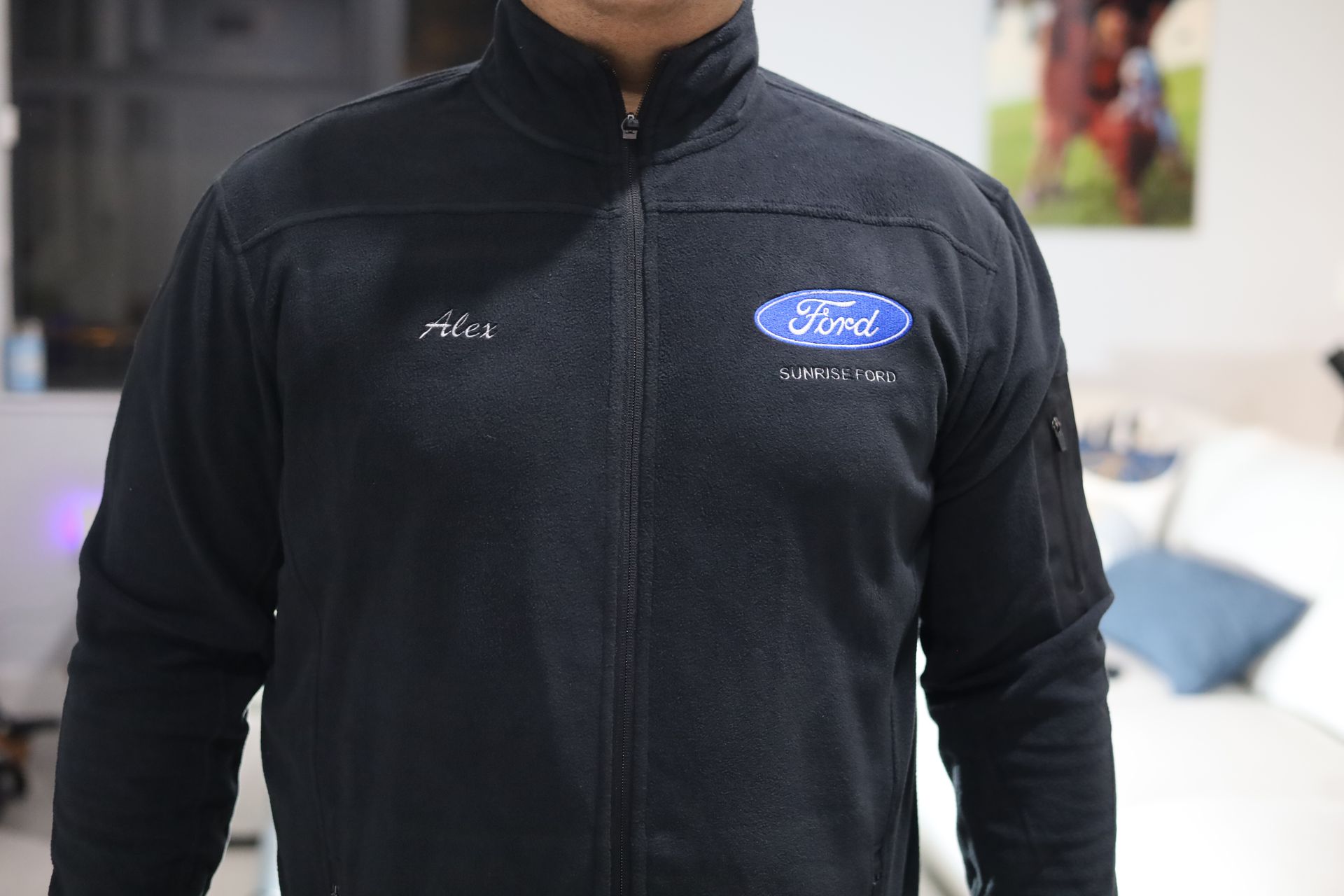 Man wearing a black Ford jacket with a logo on the chest, indoors.