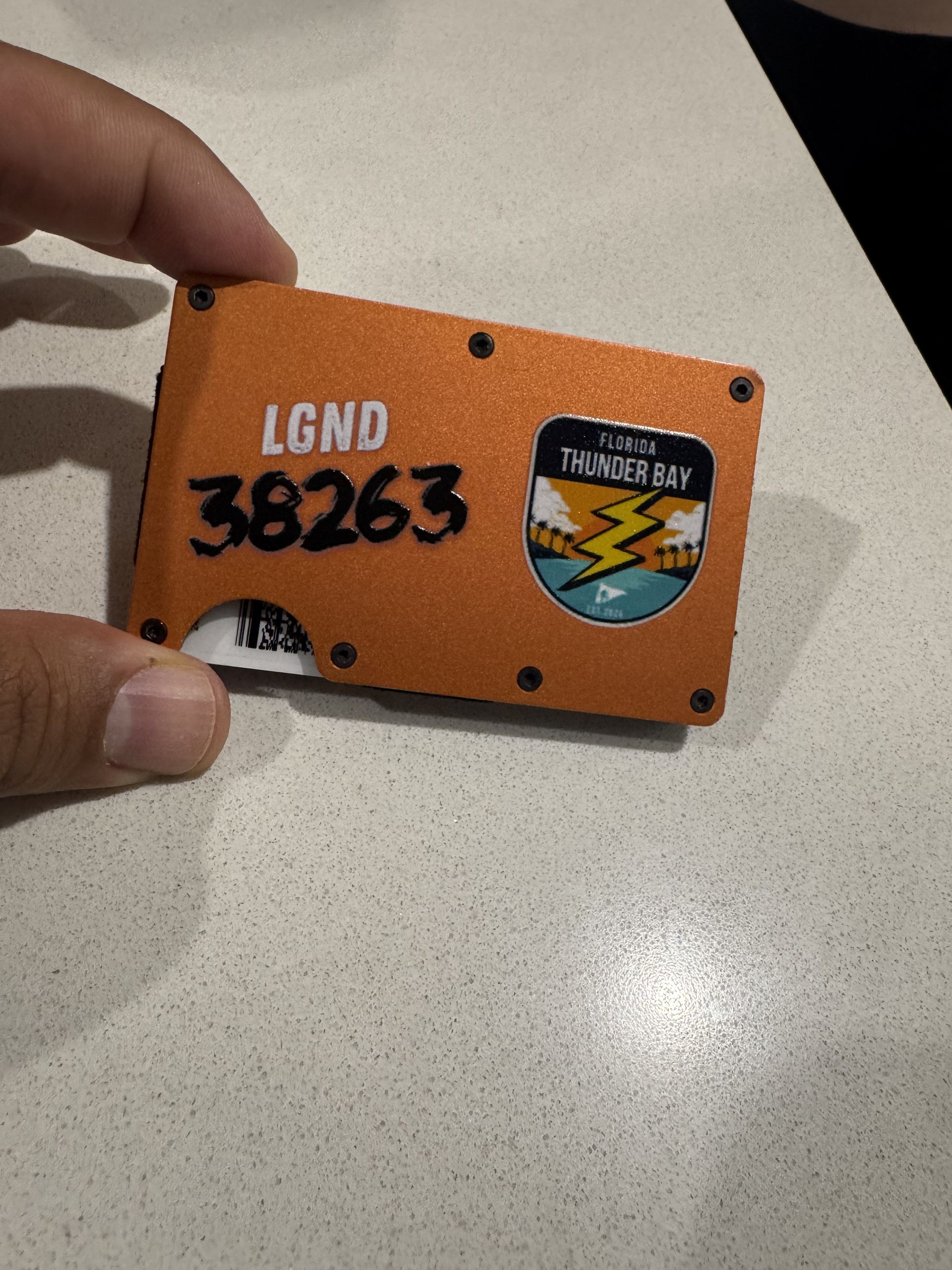 Orange wallet held by a hand, displaying "LGND 38263" and a logo for "Thunder Beach".