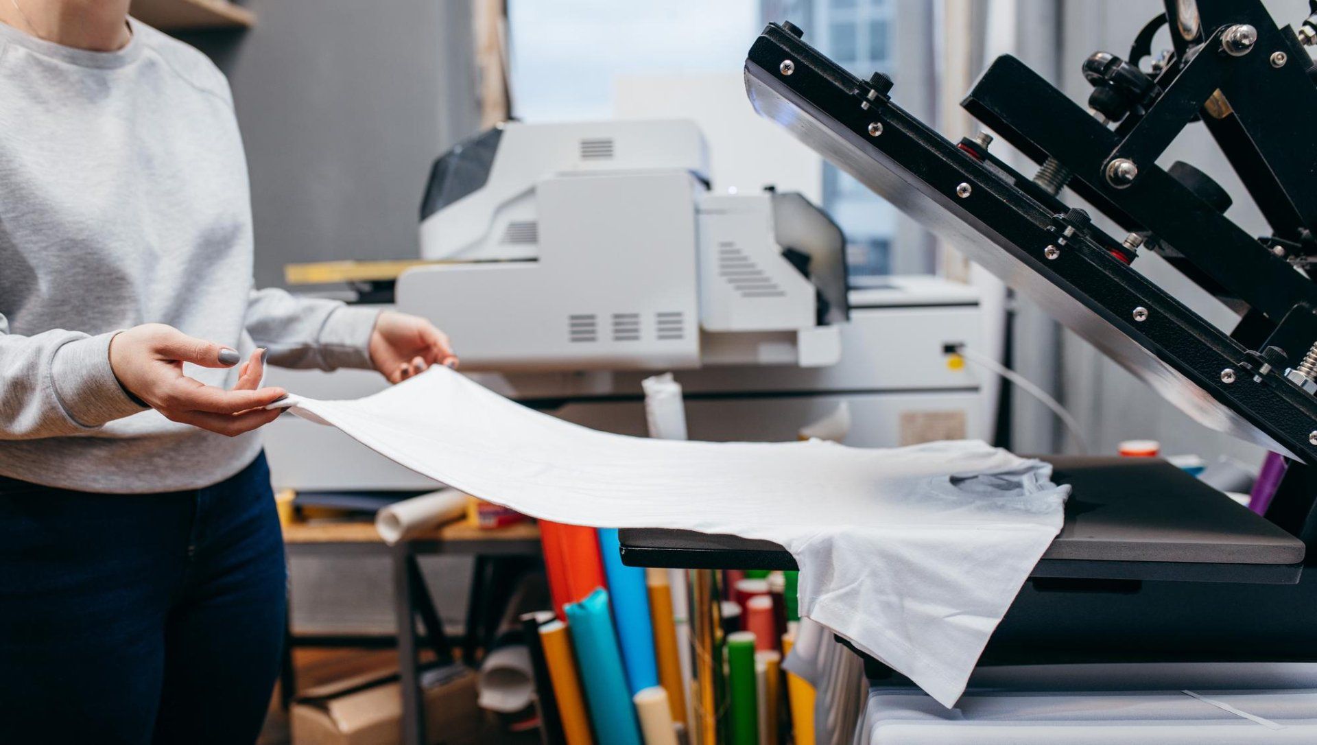 Person using a heat press machine to transfer a design onto a white t-shirt in a workshop setting.