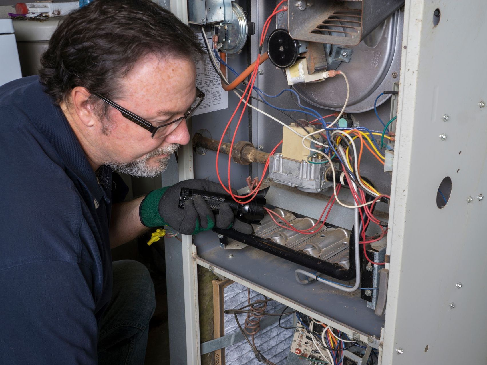 An experienced technician carefully inspecting a gas furnace, wearing protective gear and using specialized tools to ensure proper functioning and maintenance.