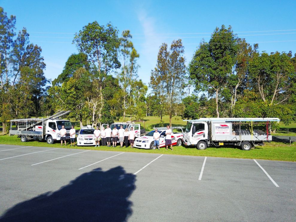A Group of People Standing Next to a Row of Trucks in a Parking Lot — Stormguard Roofing In Caloundra West, QLD