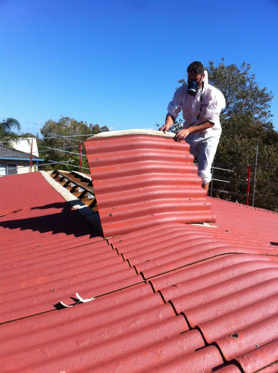 A Man is Standing on Top of a Red Roof — Stormguard Roofing In Caloundra West, QLD
