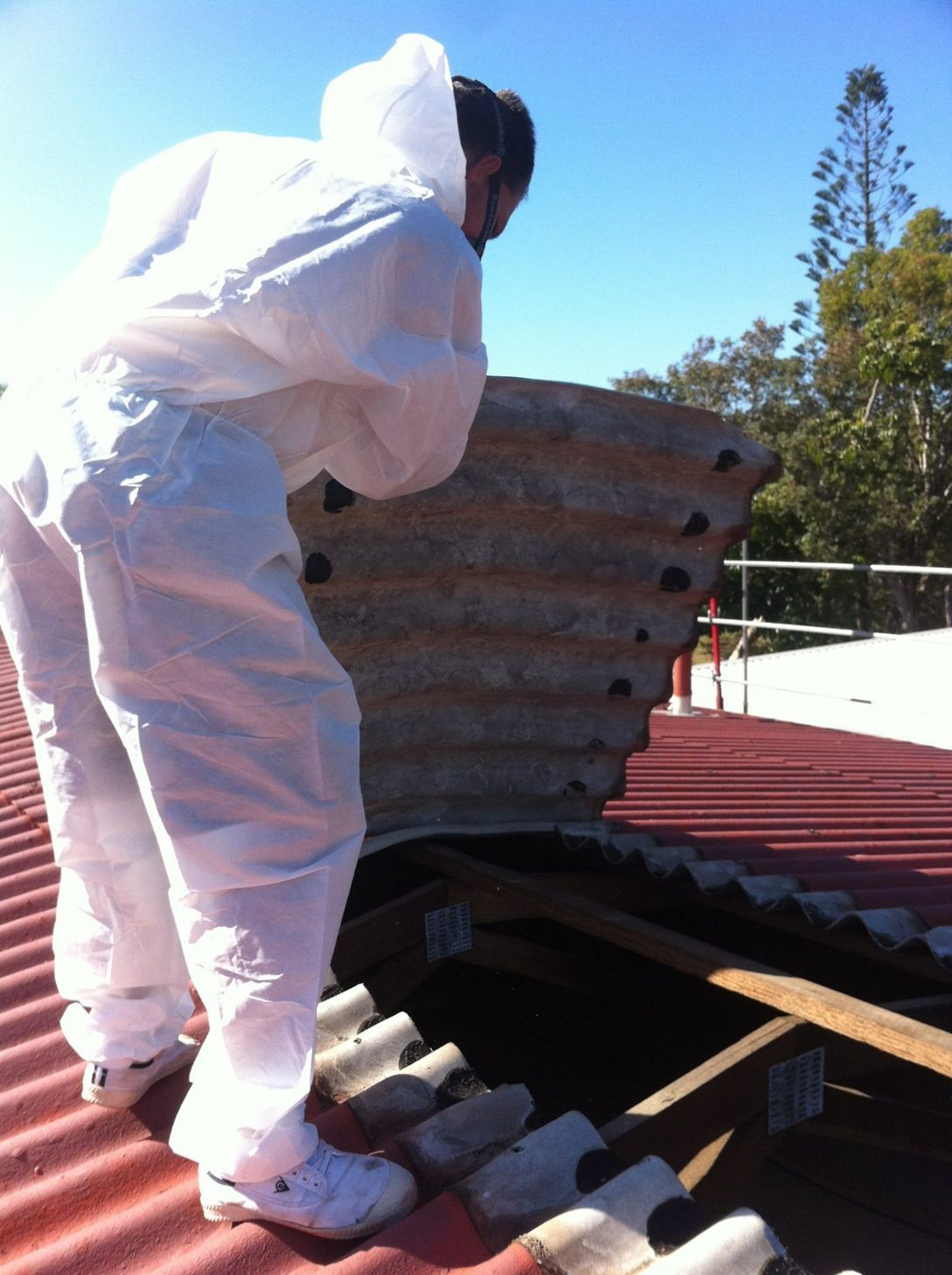A Man in a White Suit is Working on a Roof — Stormguard Roofing In Caloundra West, QLD