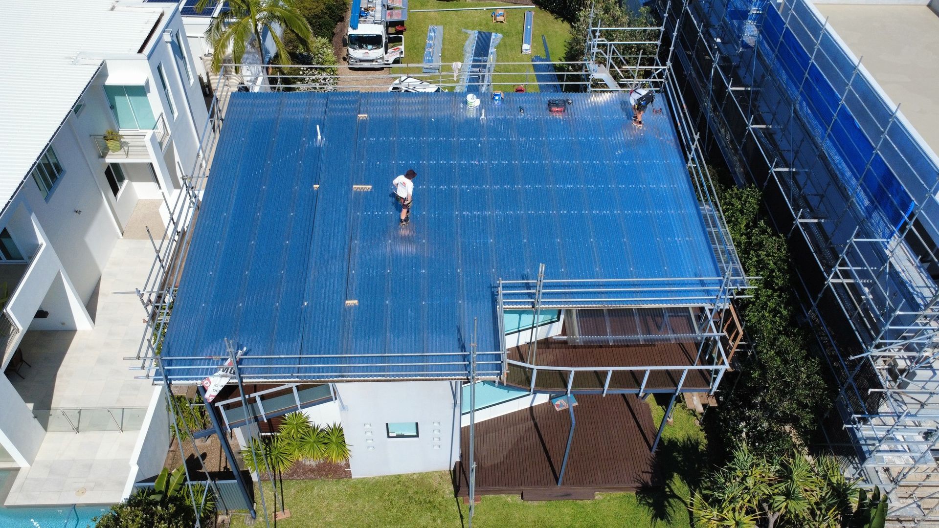 House Roof Covered in Blue Tarps With a Worker Standing on It