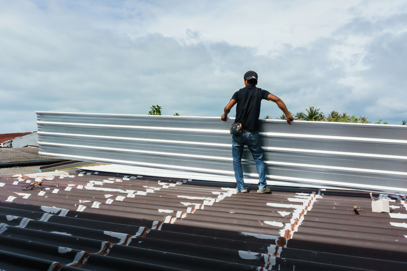 A Man is Standing on Top of a Roof Holding a Piece of Metal — Stormguard Roofing In Caloundra West, QLD
