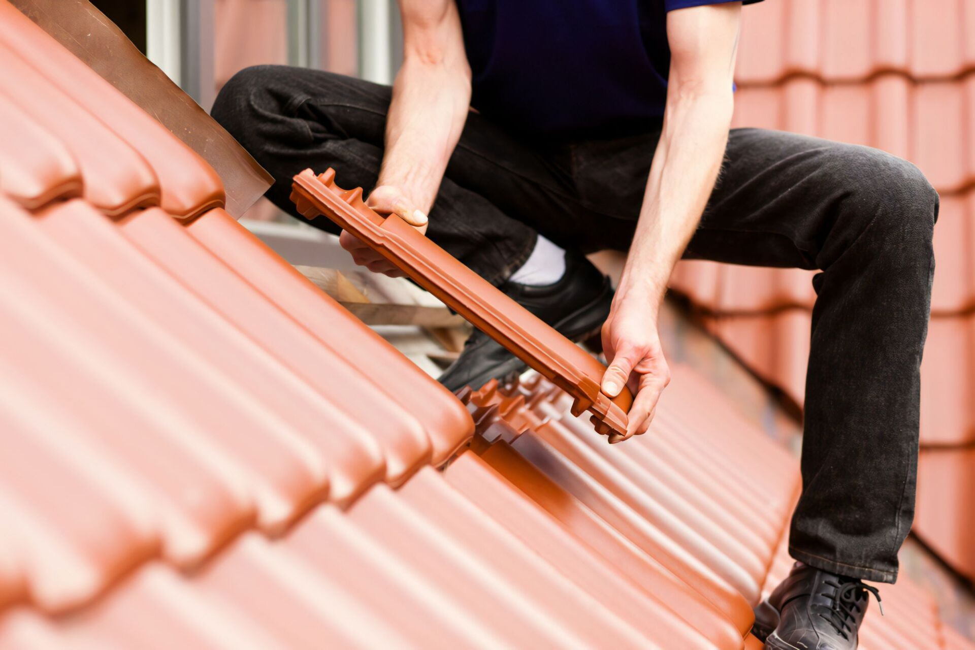 A Man is Kneeling on a Roof Holding a Piece of Tile — Stormguard Roofing In Caloundra West, QLD