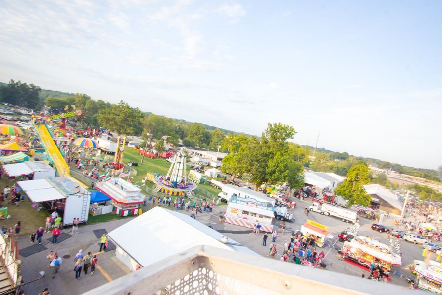 Aerial view of a colorful outdoor fair with rides, tents, and crowds on a sunny day