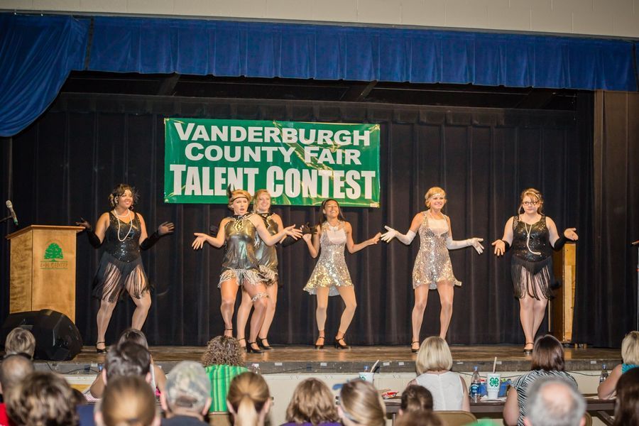 Talent contest stage with six performers in sparkly costumes under a “Vanderburgh County Fair” banner