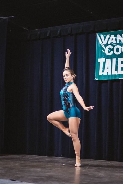 Young dancer in teal leotard posing on stage with one arm raised