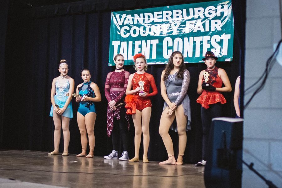 Five dancers in colorful costumes standing on a stage at Vandeburch County Fair talent contest