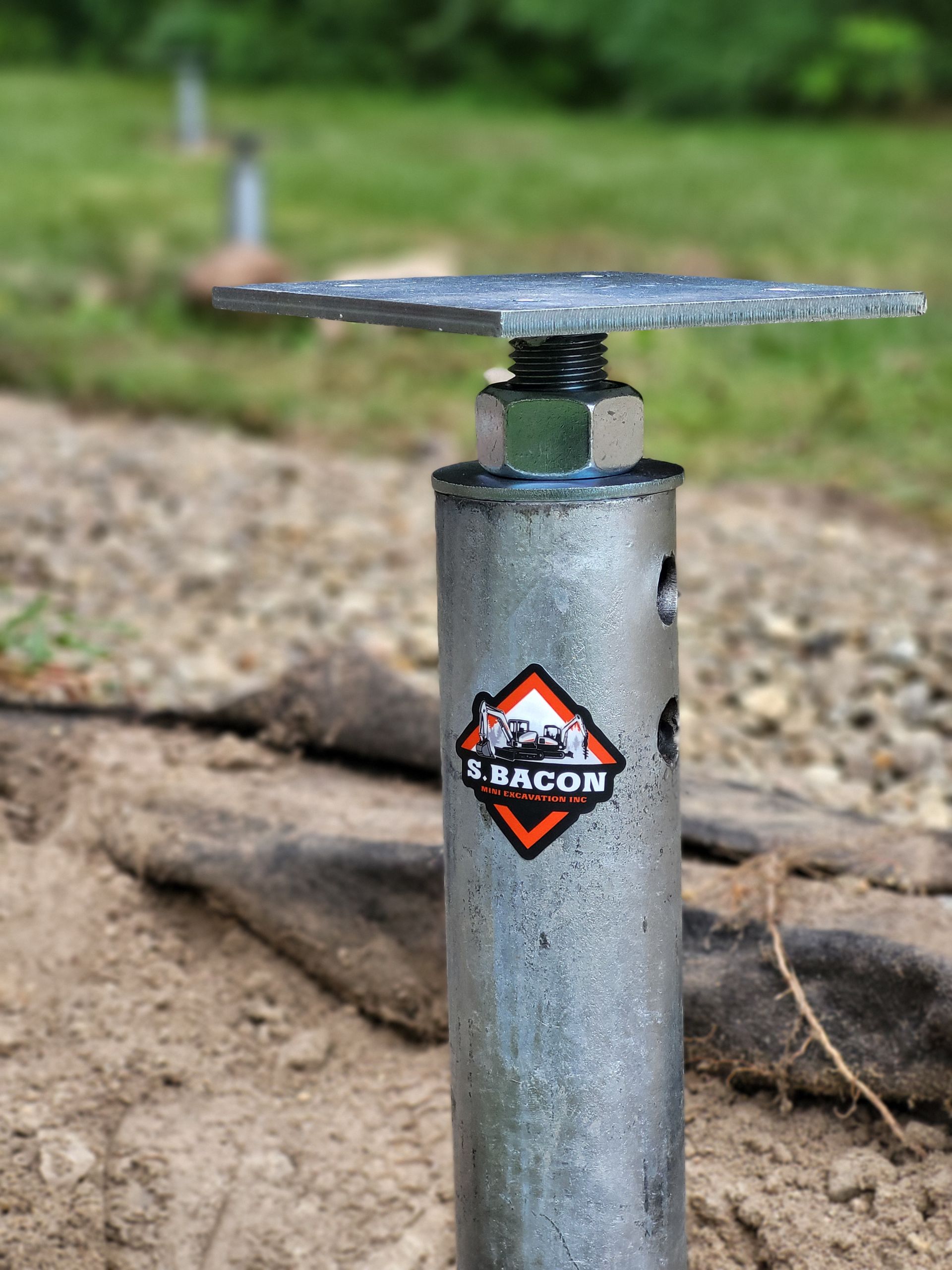 Un poteau métallique avec un écrou dessus est posé dans la terre.