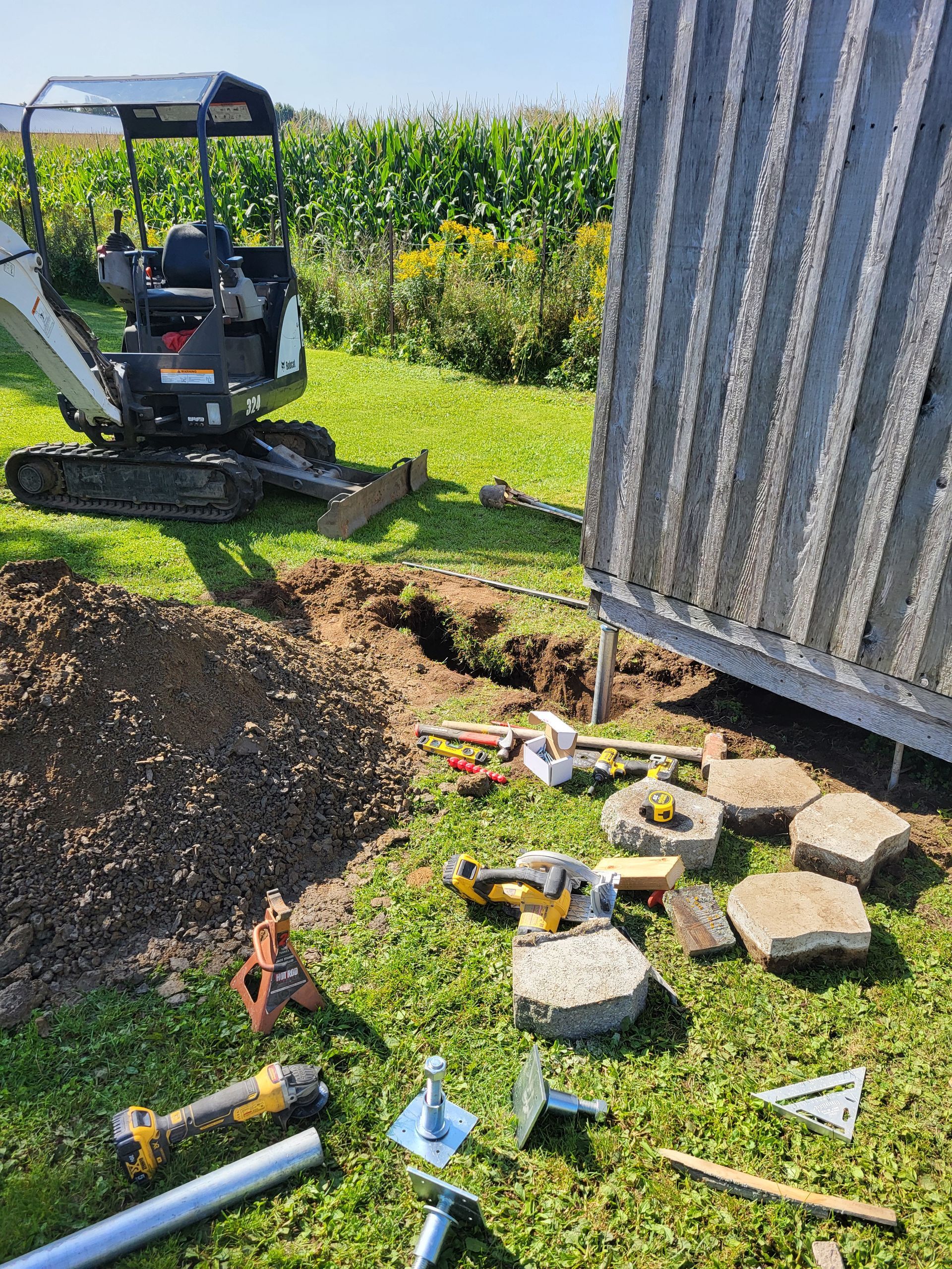 Une petite excavatrice creuse un trou dans l'herbe à côté d'un hangar.