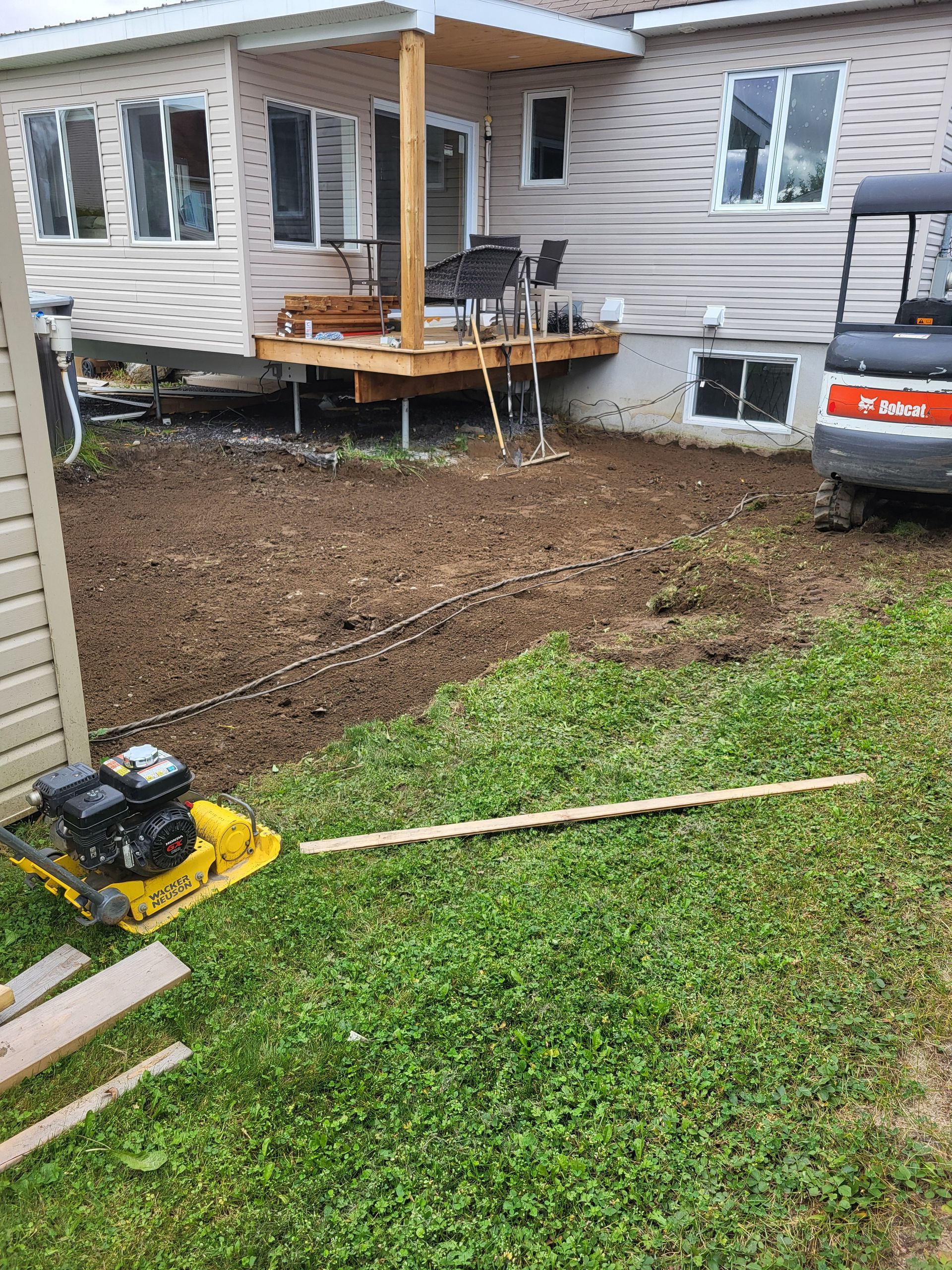 Une maison est en cours de rénovation et une petite excavatrice est garée devant elle.
