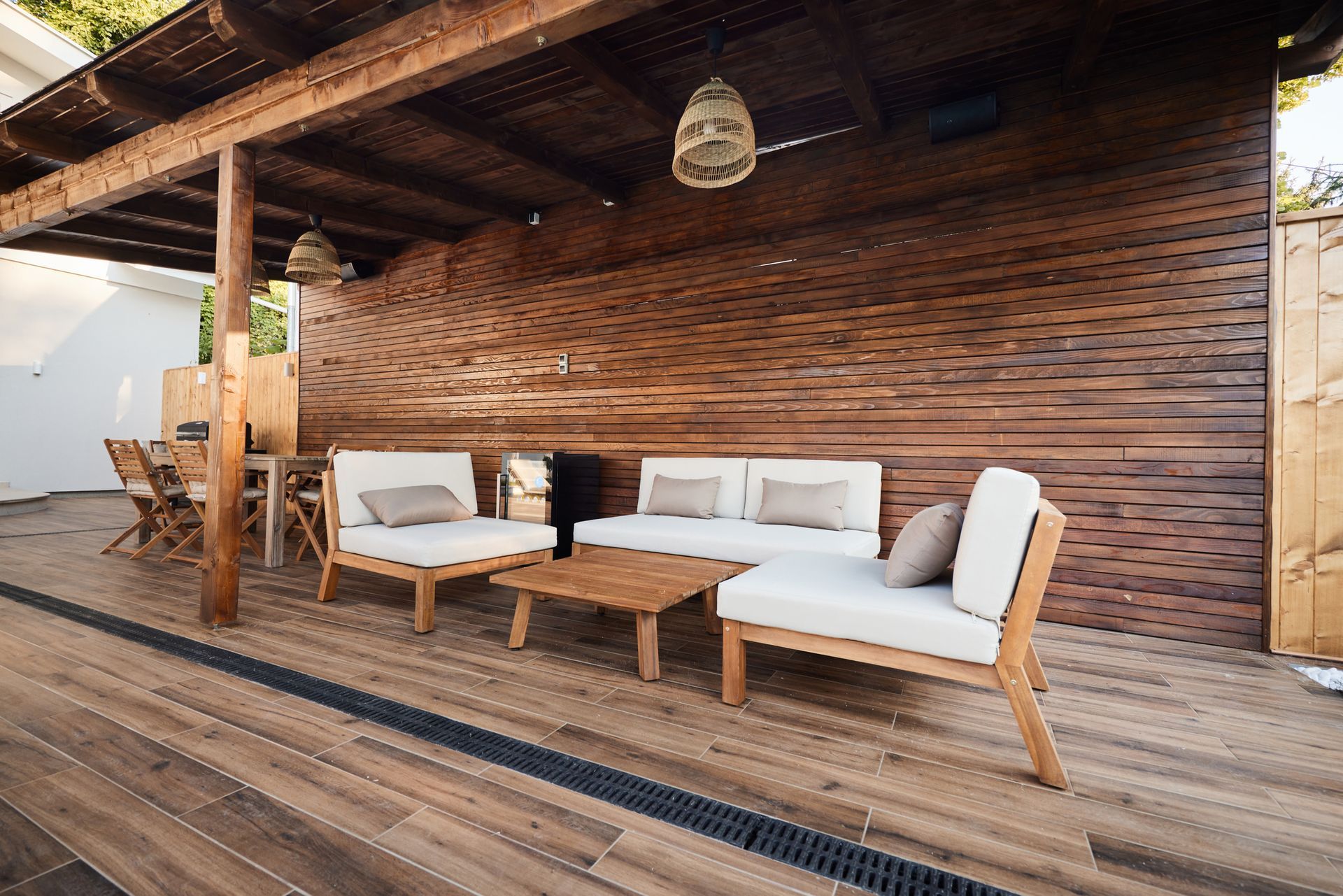 A wooden deck with a couch and chairs under a wooden roof.
