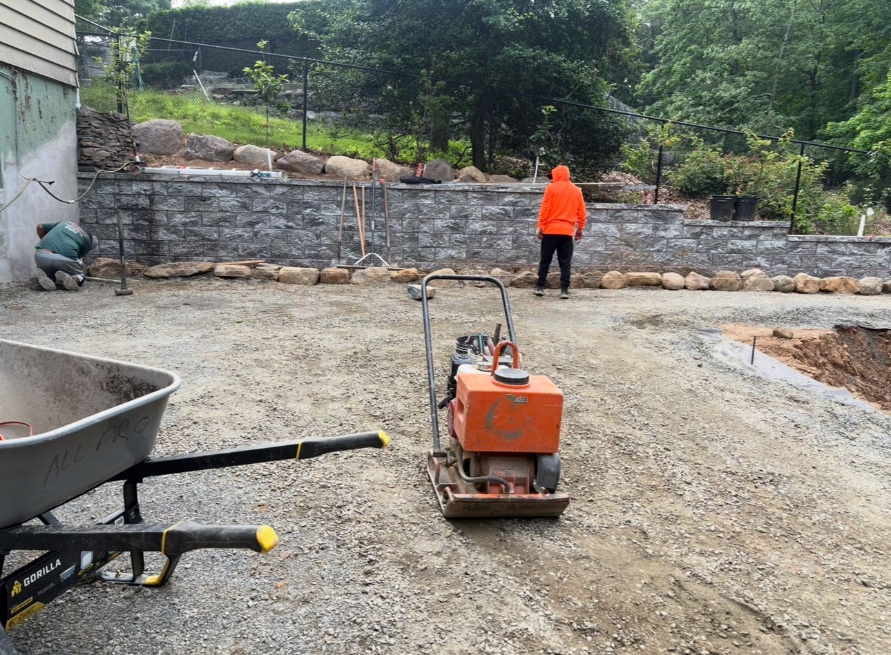 A man in an orange hoodie is working on a gravel driveway.