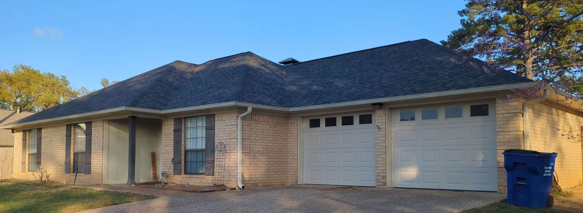 A house with two garage doors and a blue trash can in front of it.