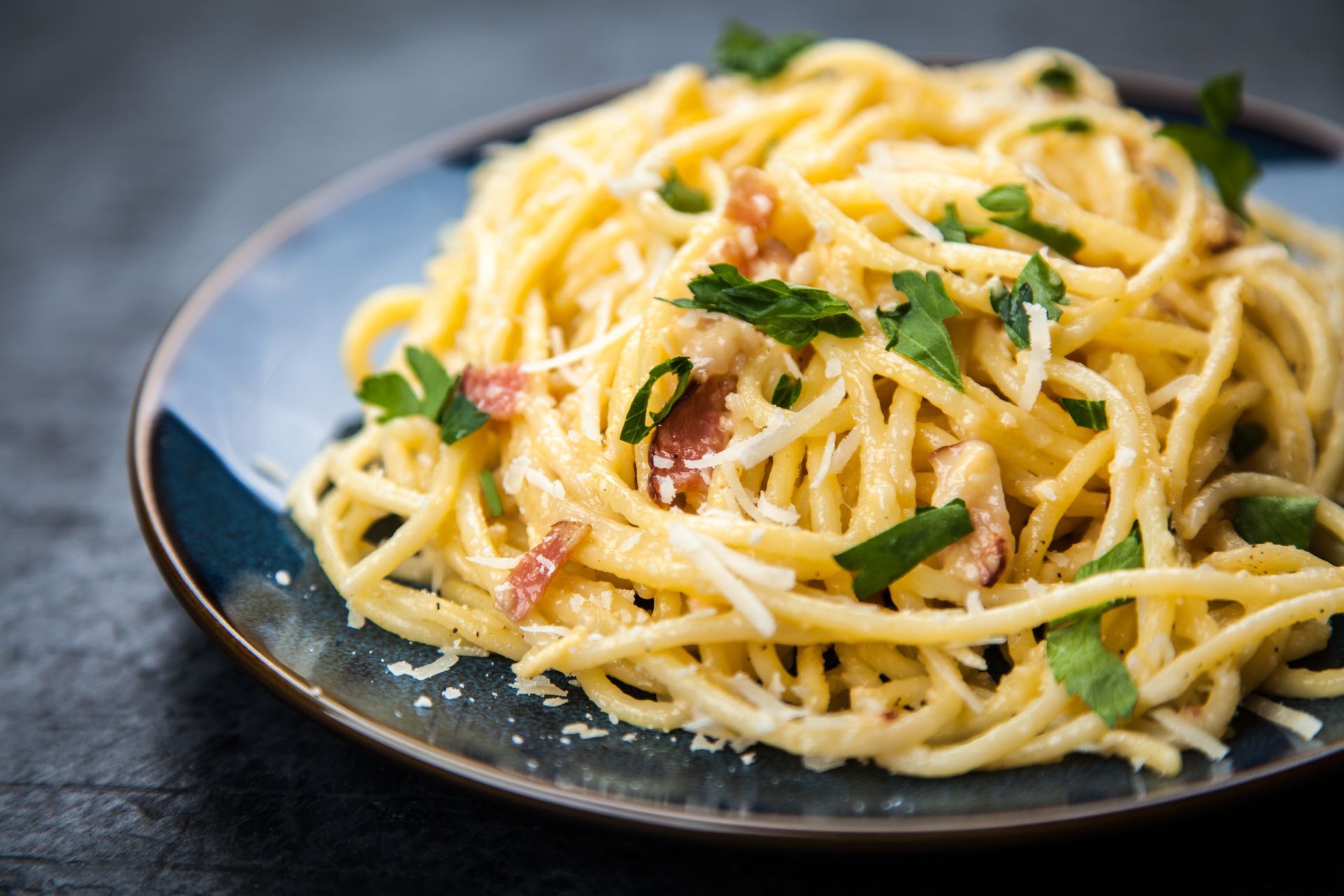 Spaghetti carbonara on a blue plate, garnished with parsley and cheese.