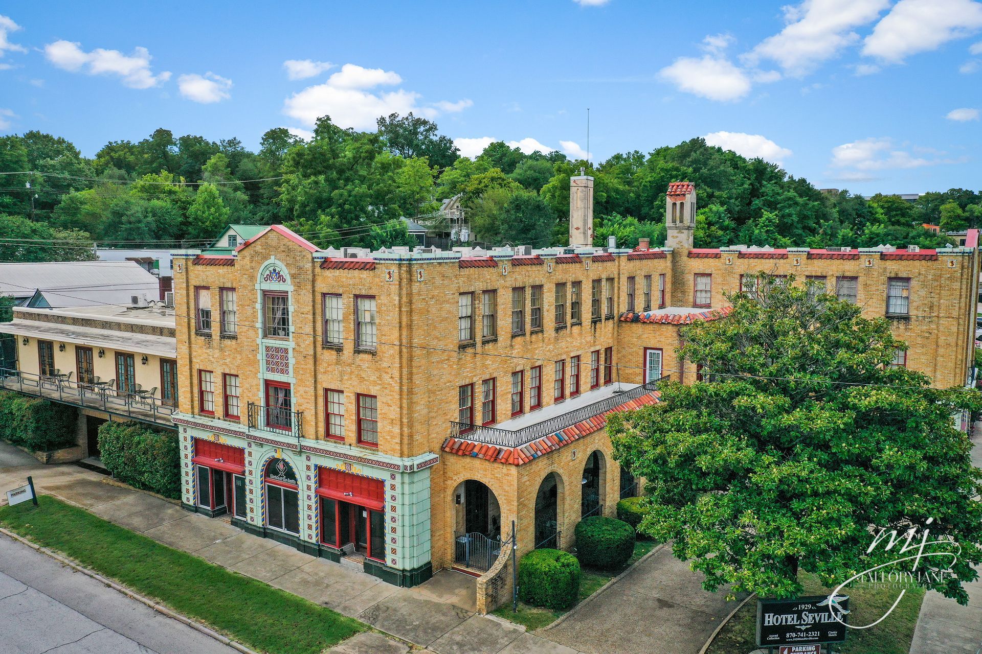 Historic brick building with arched entryway, red awnings, and tall chimney; surrounded by trees.