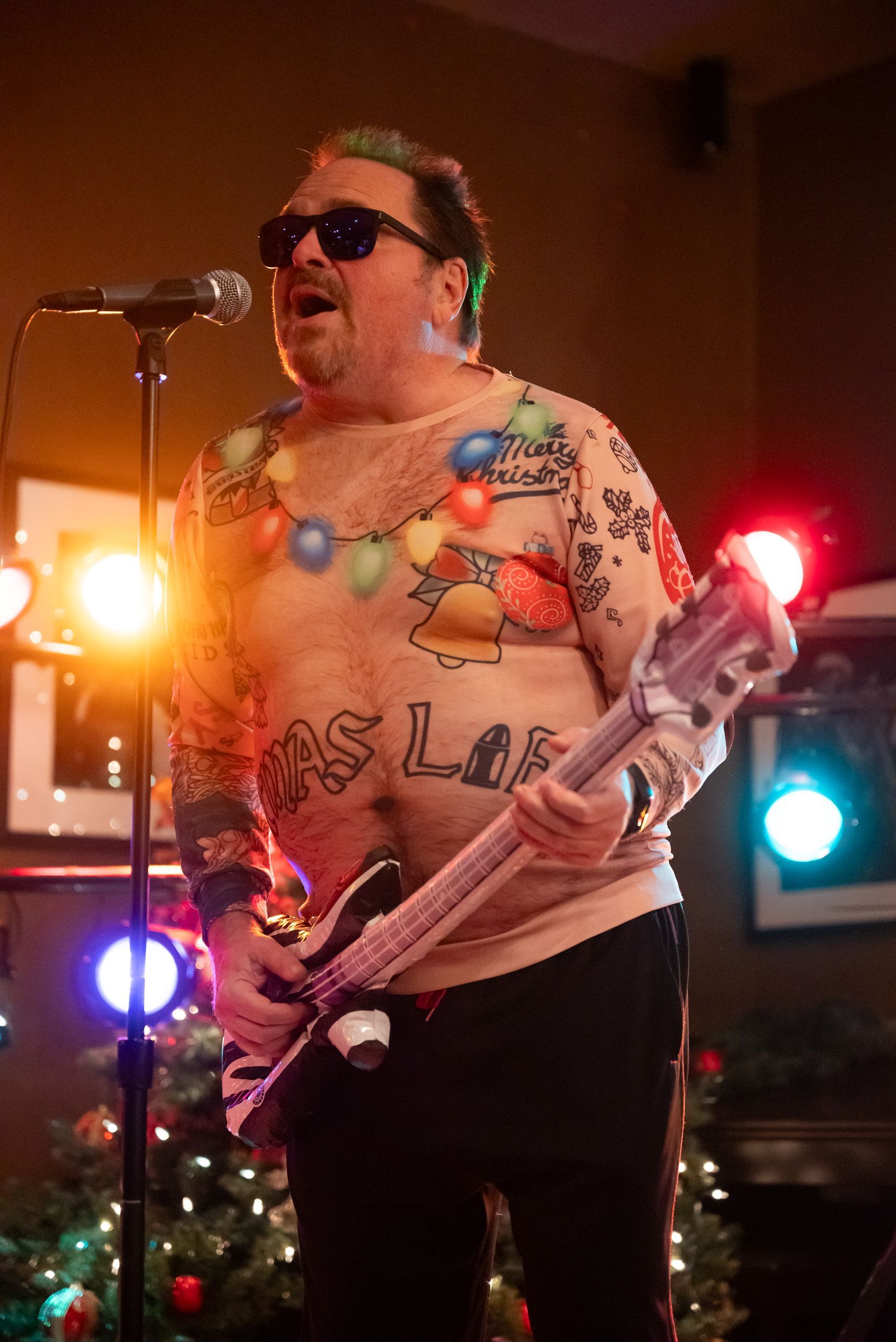 Man with guitar in novelty Christmas sweater singing on stage.