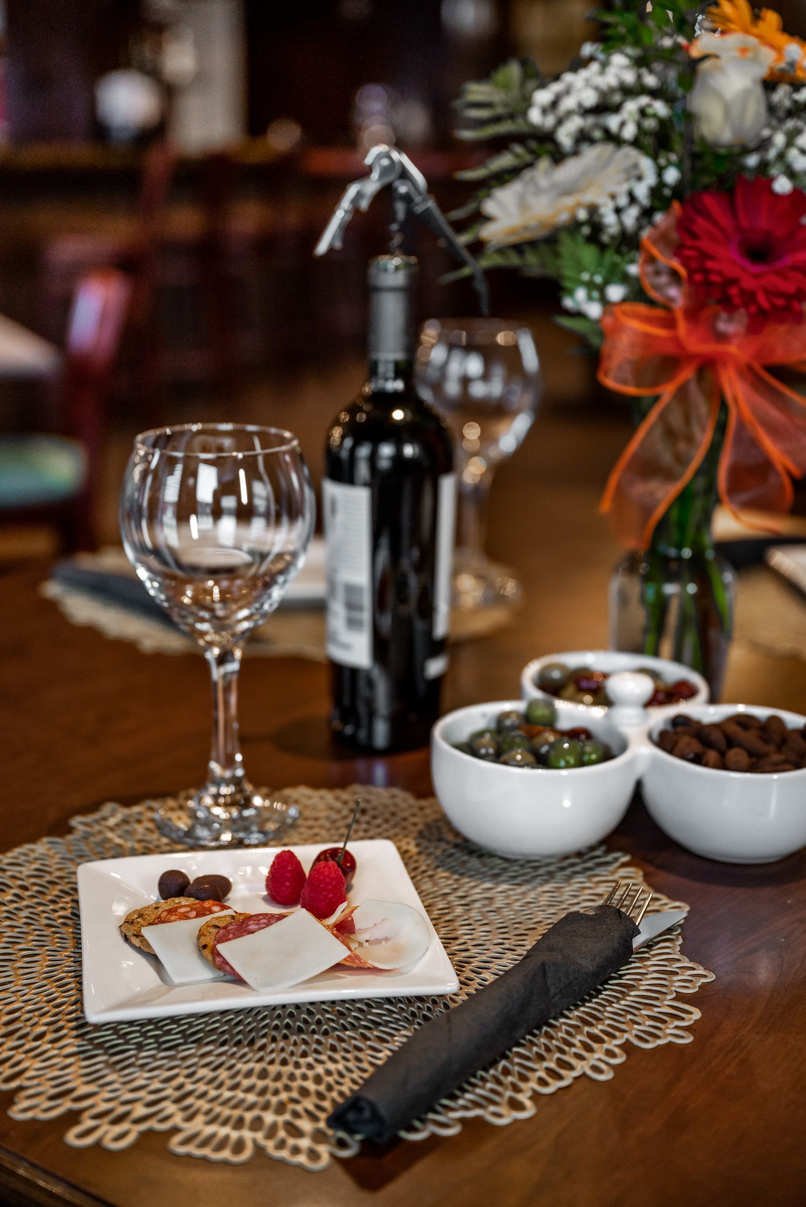 Wine glasses, bottle, food, and flowers on a table set for a meal.