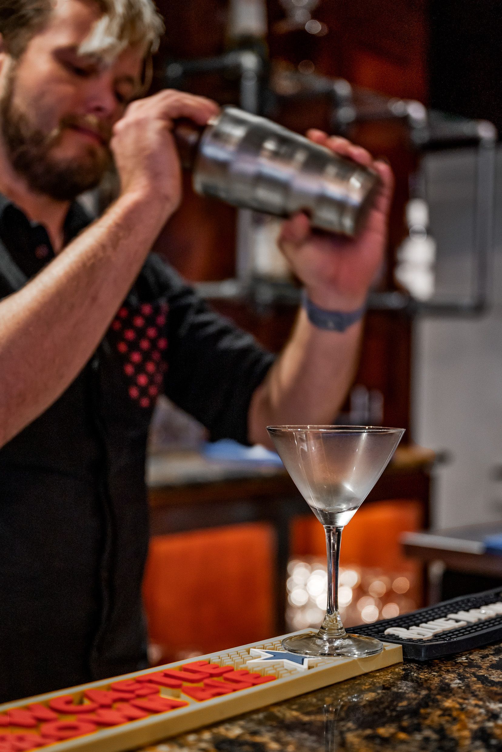 Bartender shaking a cocktail in a martini glass. Bar setting, low light.