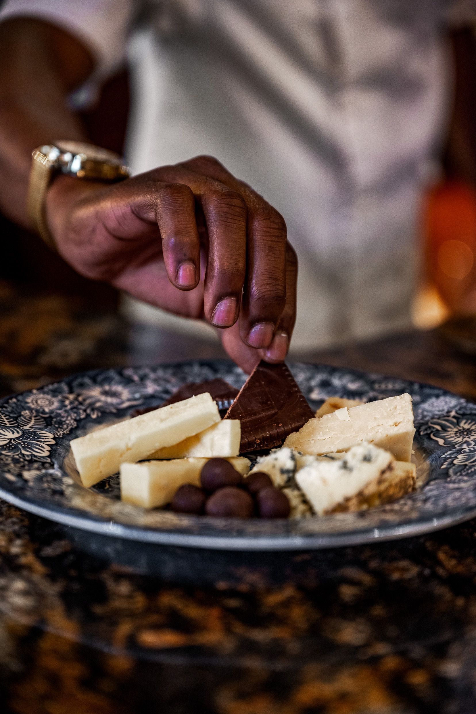 Hand reaching for chocolate on a plate with cheese and nuts.