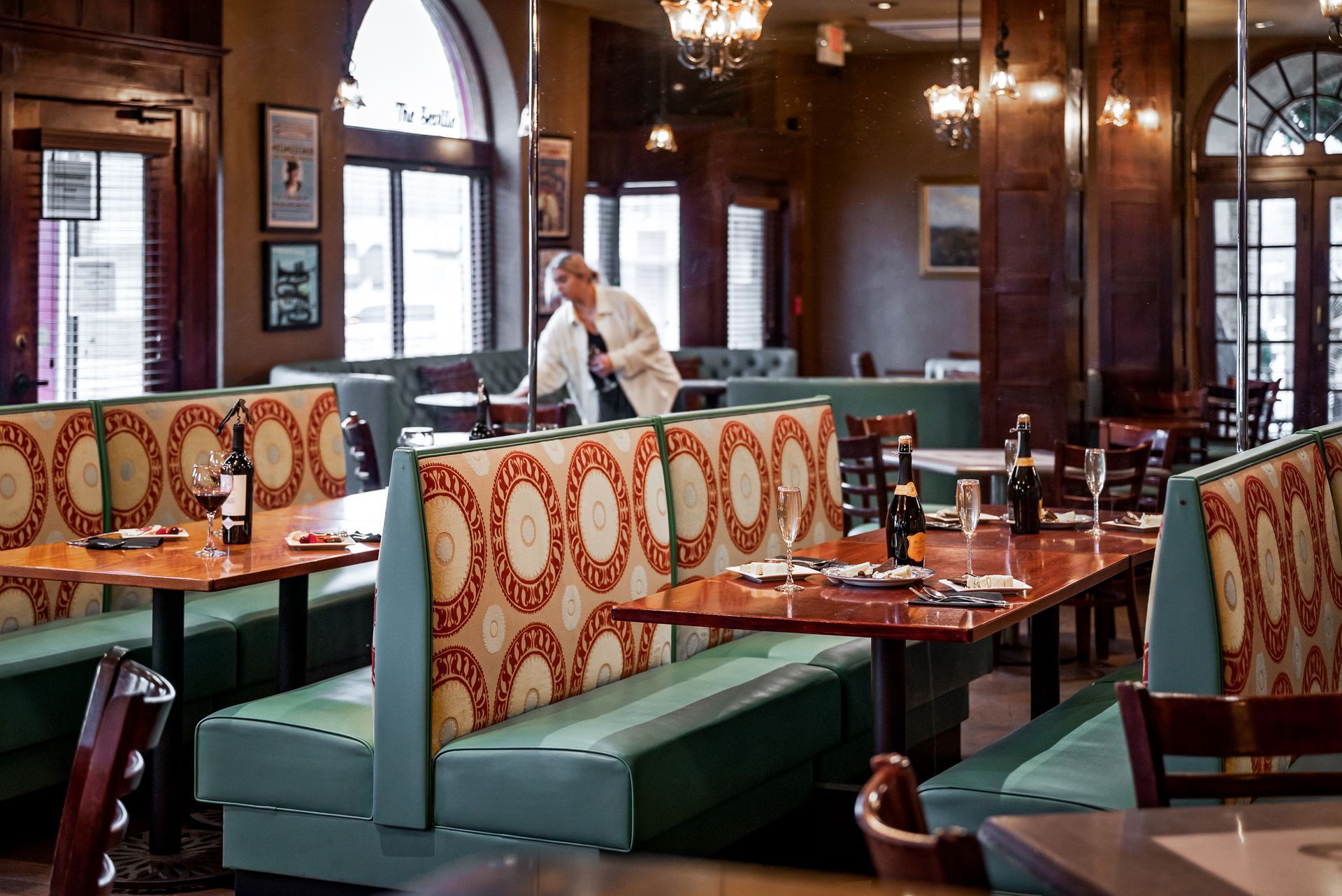 Restaurant interior with booths, tables, and a person setting a table.