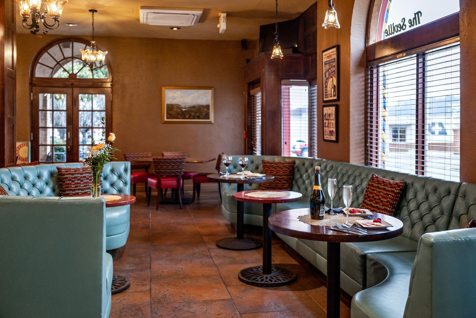 A cozy cafe interior with turquoise booths, round tables, and arched windows.