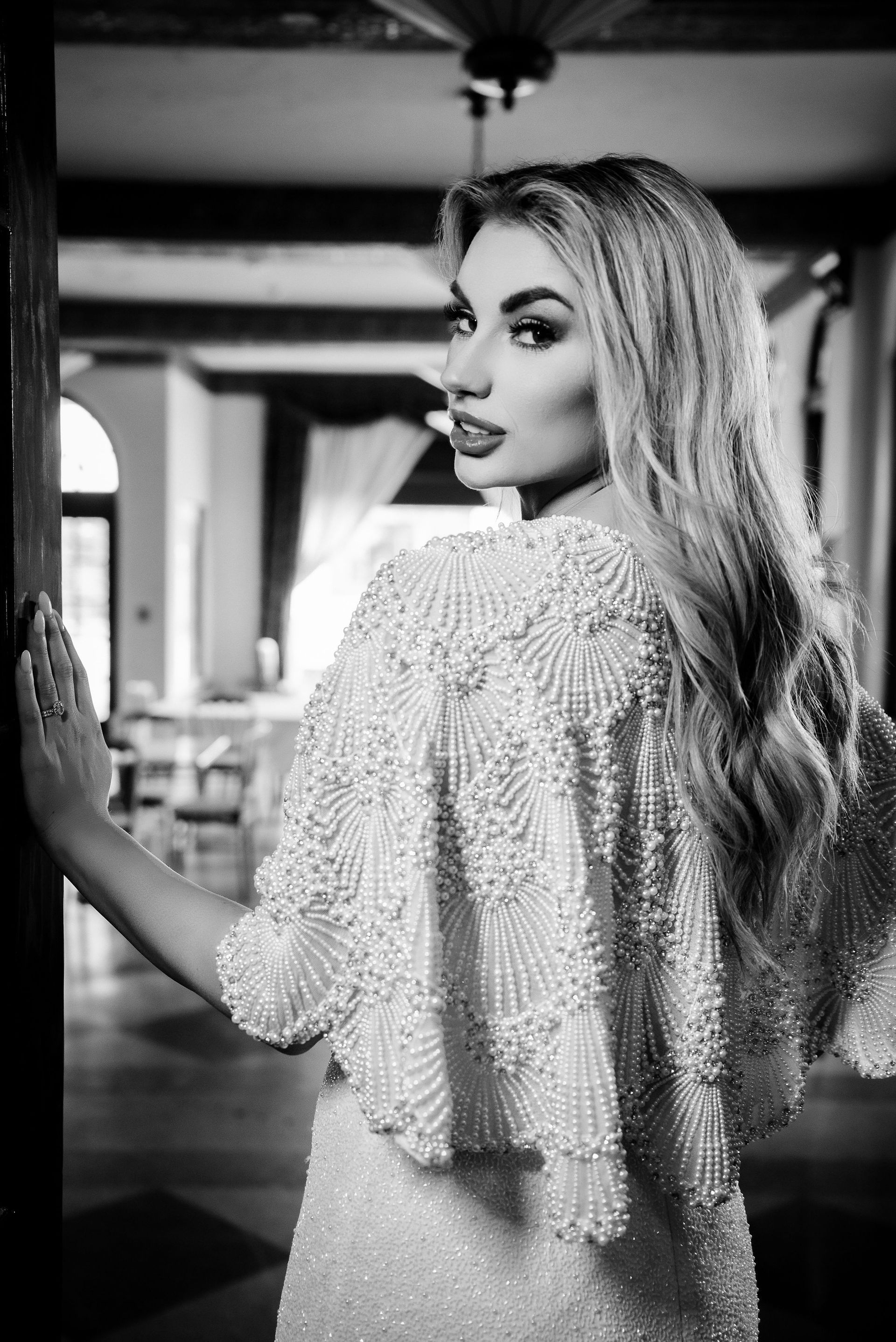 Blonde woman in beaded cape looking over shoulder, indoors.