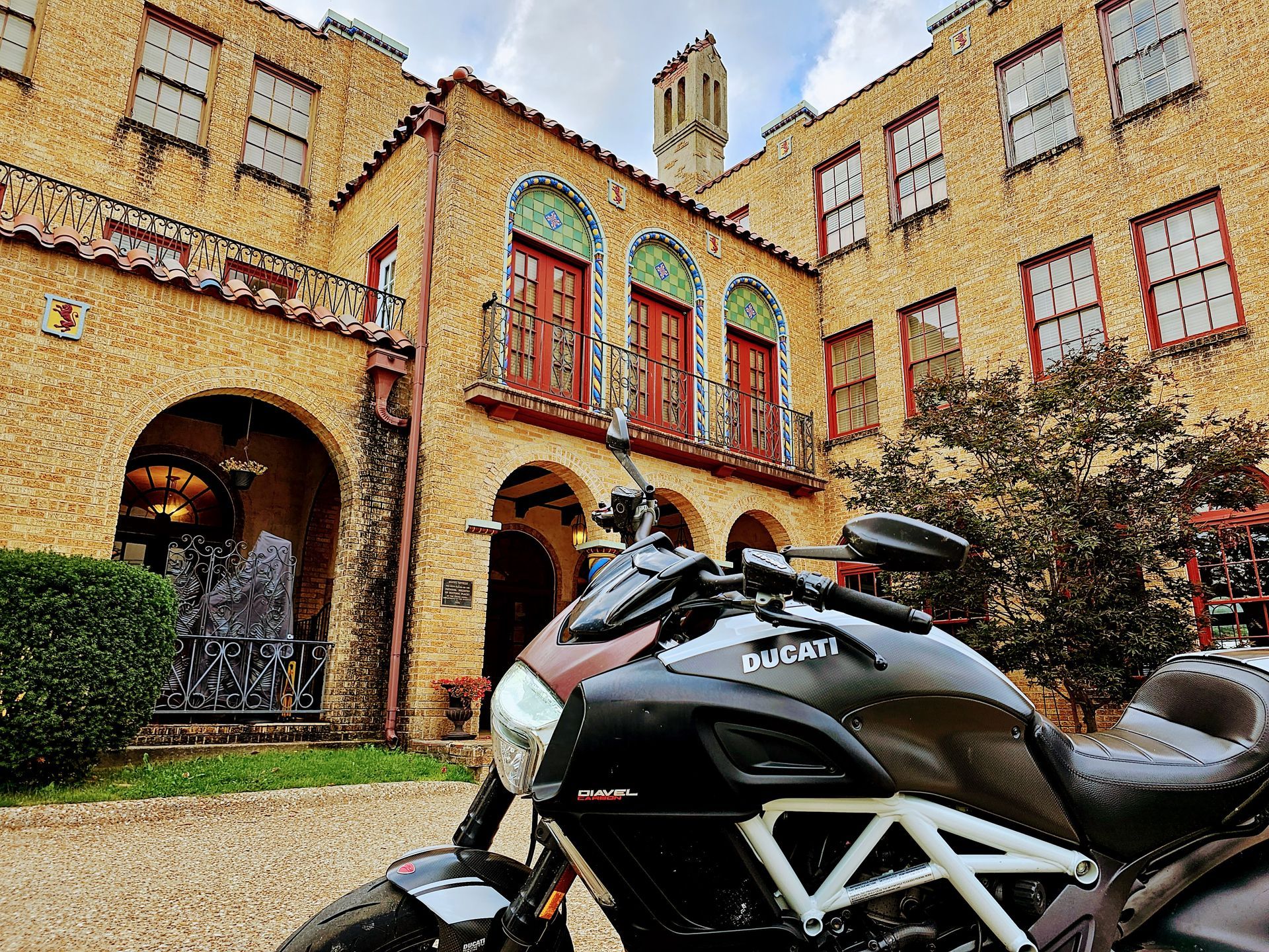 Ducati motorcycle parked in front of a yellow stucco building with arched doorways and windows.
