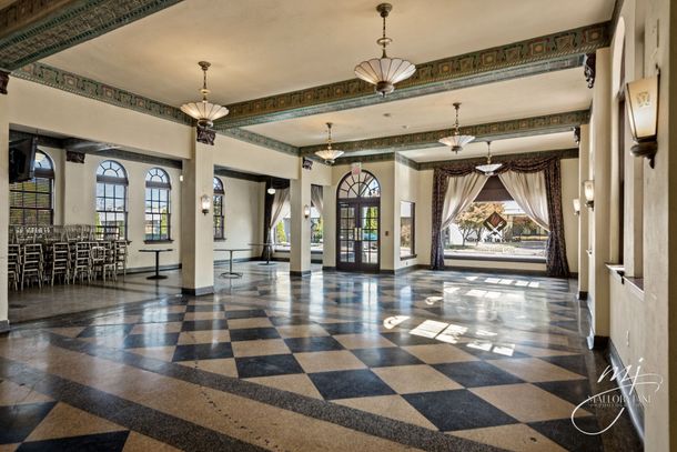 Spacious ballroom with checkered floor, large windows, ornate ceiling, and chandeliers; neutral colors.