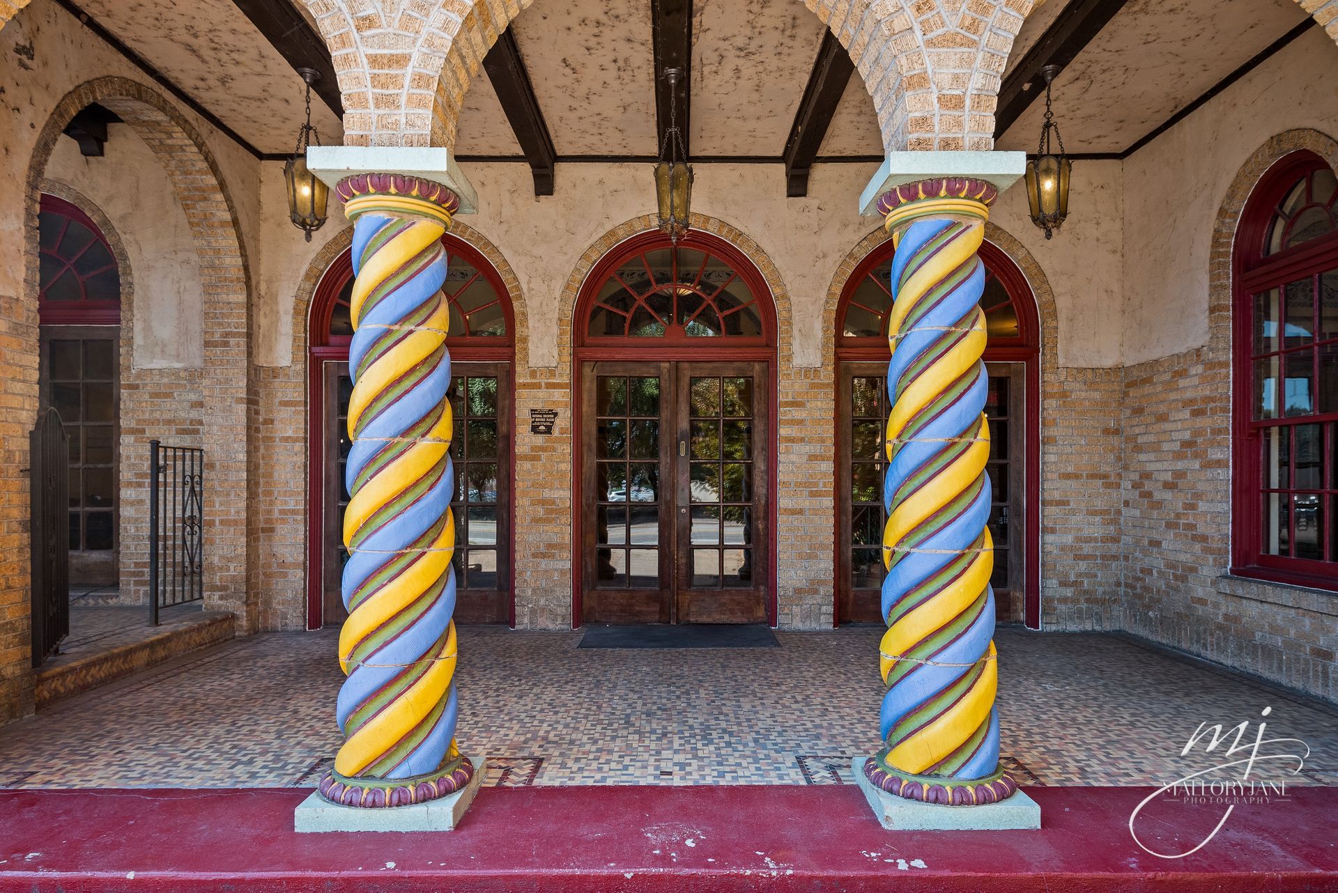 Entrance with ornate, twisted columns in blue and yellow, arched doorways, and a red carpet.