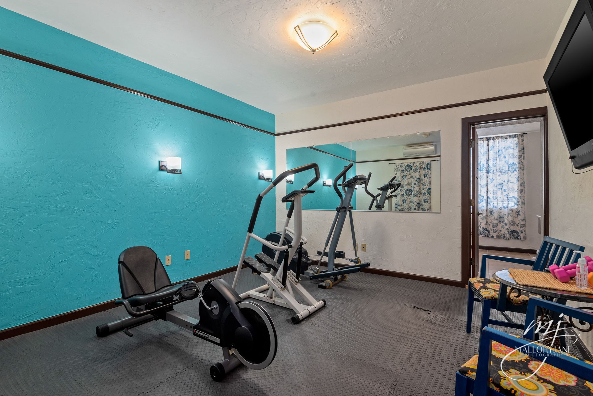 Home gym with blue accent wall, exercise equipment, mirror, and table.