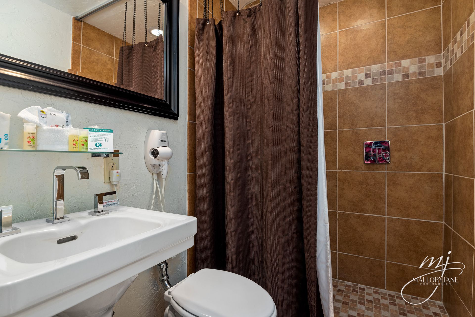 Bathroom with a white sink, toilet, and brown tiled shower behind a brown curtain.