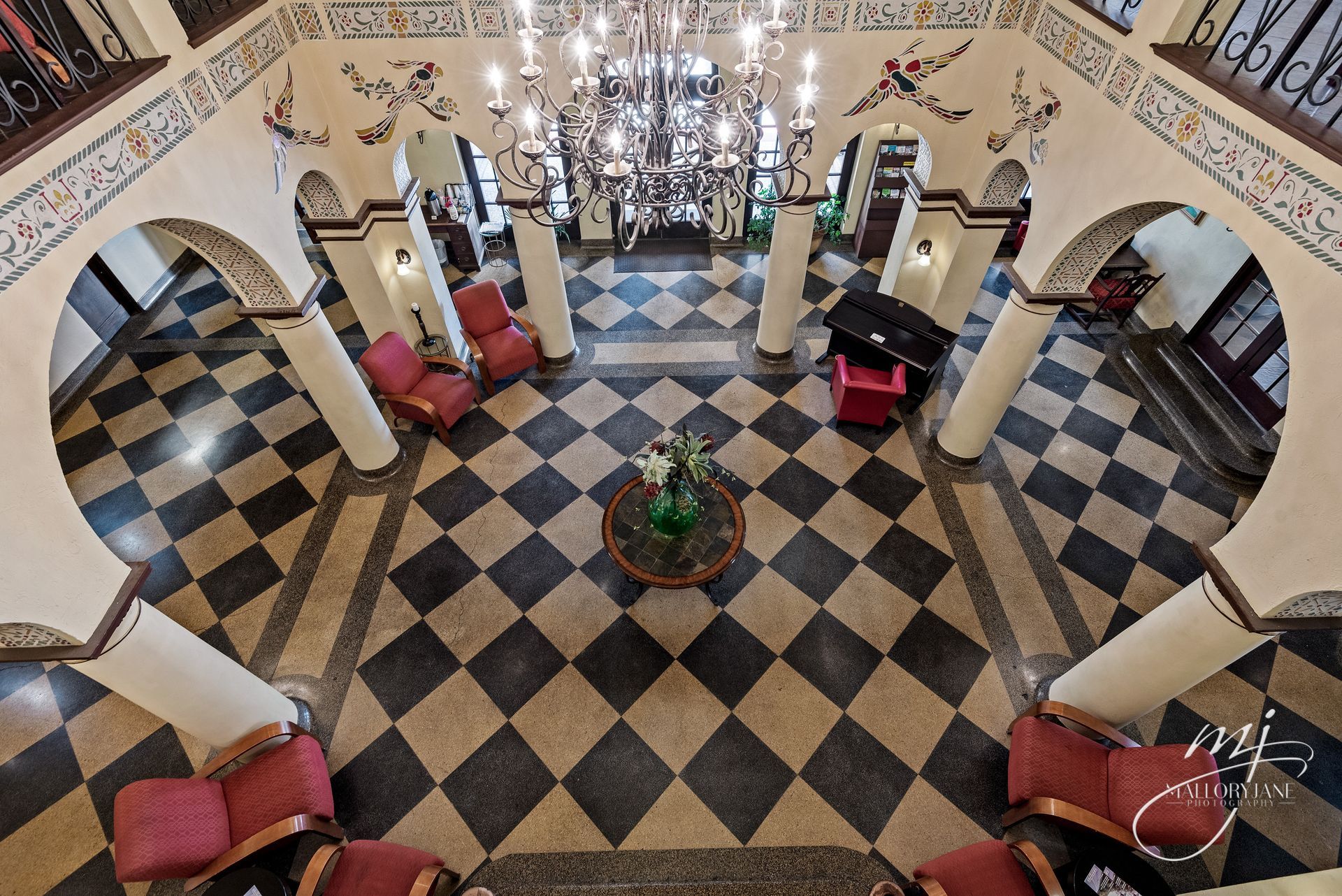 Overhead view of an ornate lobby with black and white checkered floor, red chairs, and large chandelier.