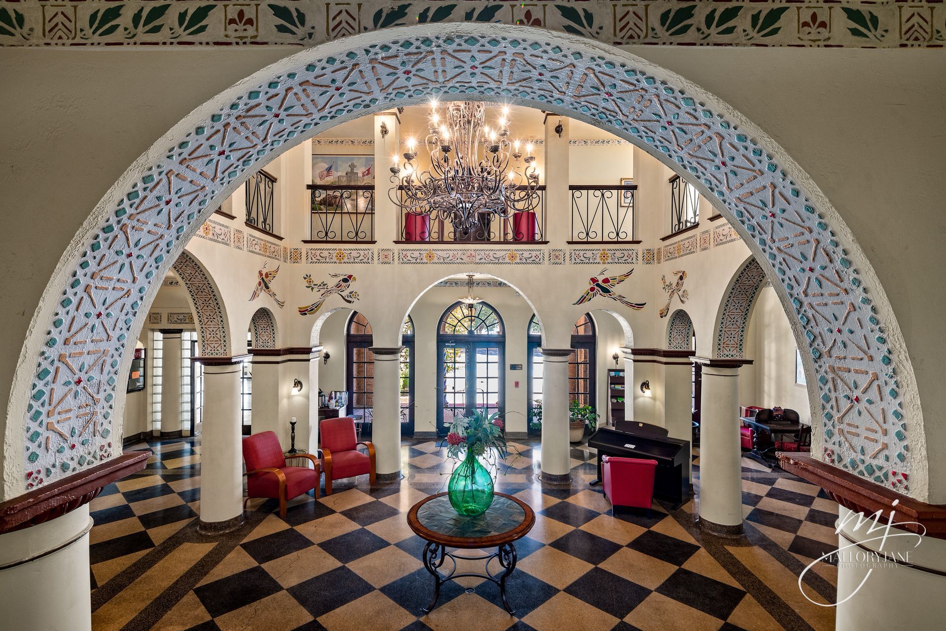 Elegant hotel lobby with arched doorway, checkered floor, red chairs, and a chandelier.