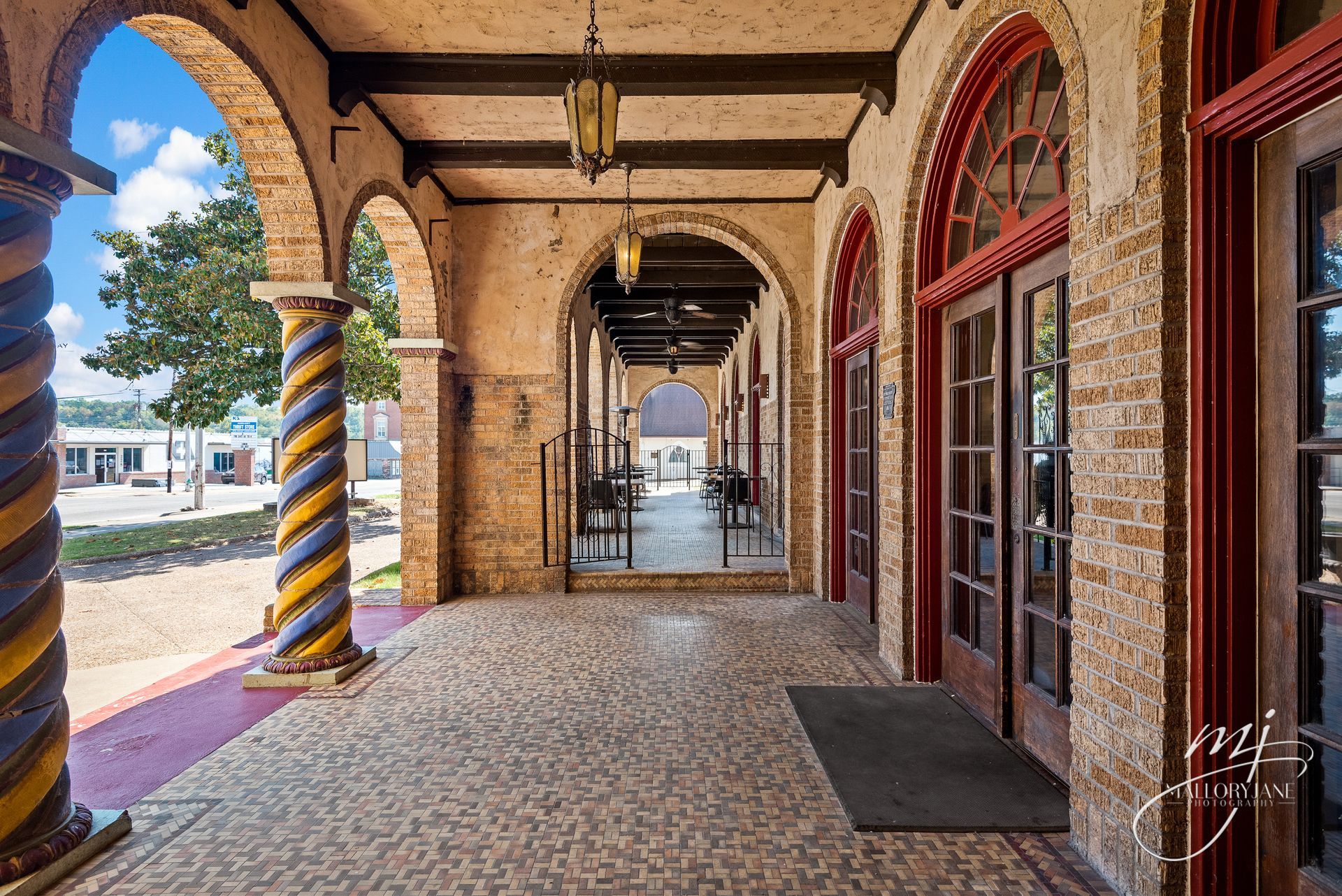 Exterior of a building with arched walkways, columns, and red-framed doors.